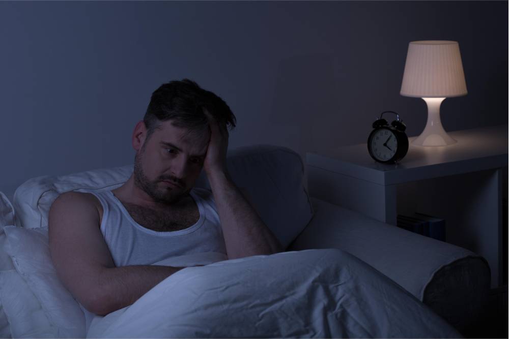 A man struggling with insomnia sits awake in bed, representing the need for Sleep Disorders Treatment in Nashville.